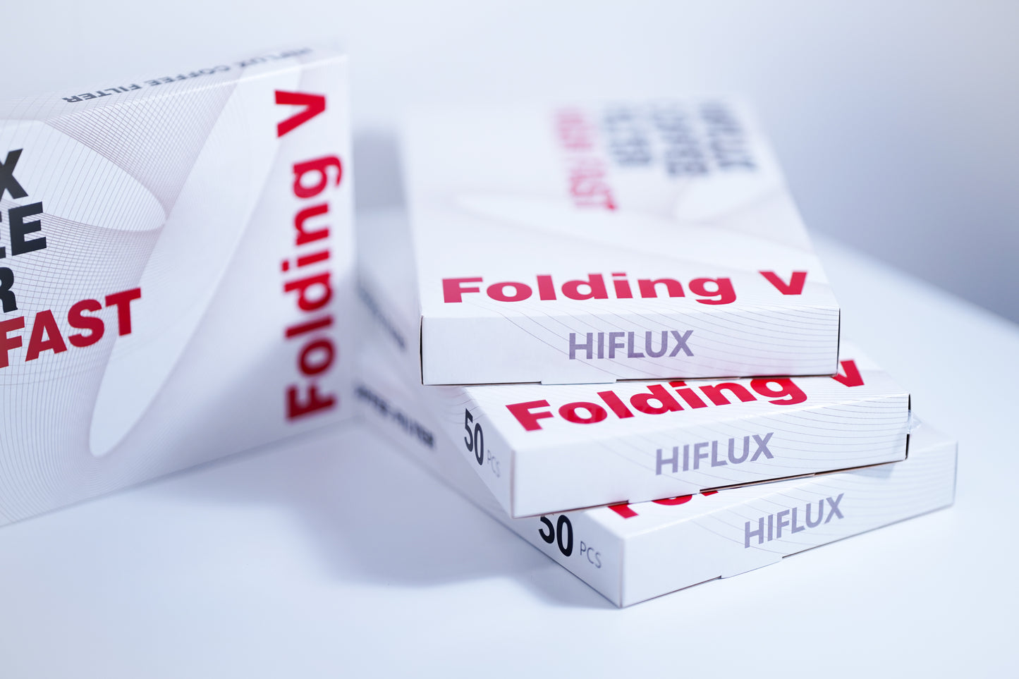 Angled shot of multiple stacked white packaging boxes for HIFLUX Folding V coffee filters, featuring red and black typography and "50 PCS" labeling